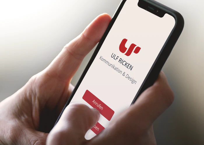 Ulf Ricken Kommunikation & Design - Webdesign Nahaufnahme von zwei Händen, welche ein Smartphone halten. Auf dem Screen des Smartphones sehen wir einen Button zur Kontaktaufnahme.